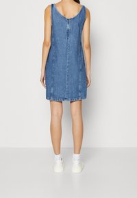 Denimmekko, jossa on avoin selkä, hihaton malli ja suora leikkaus. Vaaleansininen väri, jossa on näkyvät saumat ja teksturoitu pinta.