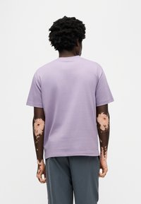 Μπλουζάκι με κοντά μανίκια σε μωβ απόχρωση λεβάντας, κατασκευασμένο από μαλακό βαμβάκι, με κλασικό στρογγυλό γιακά και χαλαρή εφαρμογή, με εμφανή υφή και ραφές.