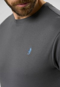Pilka medvilninė marškinė su apvaliu kaklu, su nedideliu mėlynu išsiuvinėtų figūros su skrybėle logotipu kairėje krūtinės pusėje.
