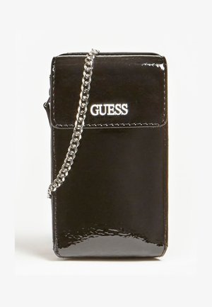Petit sac bandoulière en cuir verni noir avec une chaîne argentée et le logo "GUESS" sur le rabat avant.