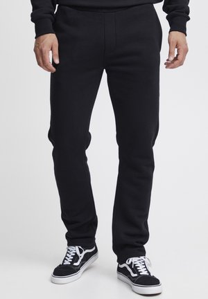 Pantalones de chándal negros en corte slim, con una textura suave, detalles de costura y una cinturilla elástica, combinados con zapatillas negras y blancas.