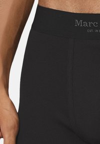 Schwarze gerippte Boxershorts mit einem breiten schwarzen Bund, der den Markennamen in grauem Text zeigt, betont eine glatte Textur und eine enge Passform.