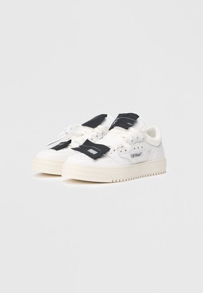 Adidași albi din țesătură și cauciuc, cu o talpă groasă, etichete negre, design minimalist și detalii perforate.