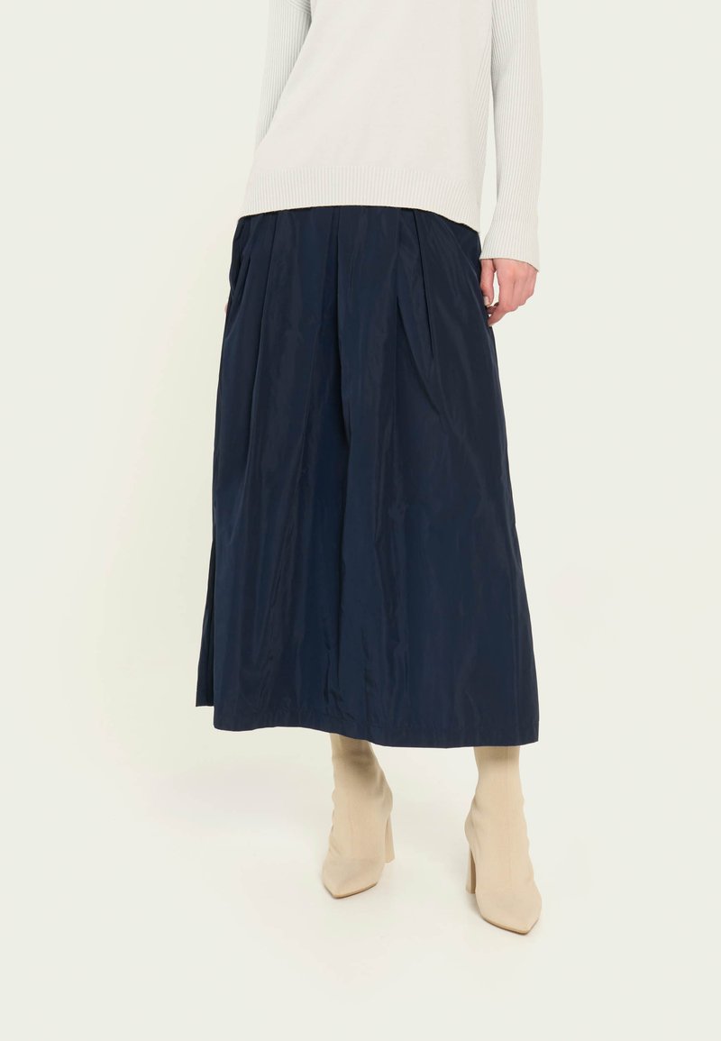 Falda midi azul marino con pliegues, hecha de una tela suave, combinada con botas de calcetín beige. La parte de arriba es de punto de color claro.