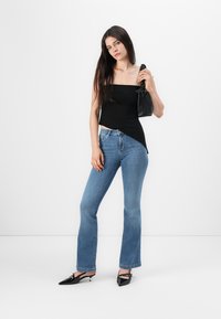 Svart åtsittande strapless-top, blå utsvängda jeans, svart handväska och spetsiga skor. Släta texturer och en avslappnad stil som visas mot en vit bakgrund.