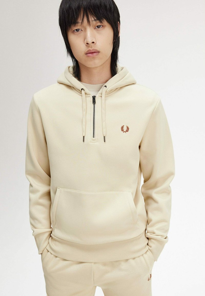 Felpa beige con tasca frontale e mezza cerniera, realizzata in tessuto morbido. Presenta un piccolo logo ricamato marrone sul petto.