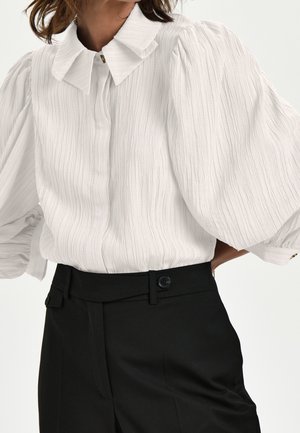 Weiße strukturierte Bluse mit Puffärmeln und einem einzigartigen gefalteten Kragen, kombiniert mit hoch taillierten schwarzen Hosen mit Knopfdetails.