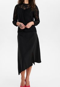 Top nero con maniche in pizzo, abbinato a una gonna nera asimmetrica con uno spacco laterale, completato da vivaci tacchi rosa.