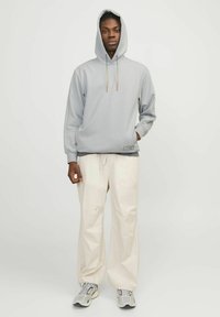 Lys grå hoodie med en snoretræk hætte, med lange ærmer og en syet detalje ved kanten, parret med cremefarvede wide-leg bukser.