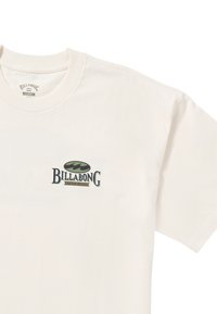 Cremefarvet bomulds t-shirt med et grønt og sort Billabong-logo på fronten, rund hals og korte ærmer.