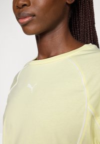 Geel sporttop met een ronde halslijn, witte details bij de naden, en een wit Puma-logo dat op de linkerborst is geplaatst.