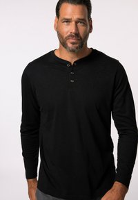 T-shirt henley noir à manches longues, avec une patte de boutonnage à trois boutons, une texture douce, et un logo en relief subtil sur la poitrine.