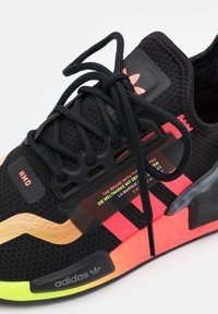 Black athletic shoe with textured fabric, neon orange and pink accents, thick soles, black laces, and multi-language branding on the side.