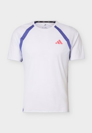 Biała sportowa koszulka Adidas z krótkim rękawem, z fioletowymi akcentami na ramionach i małym czerwonym logo Adidas na lewej piersi.