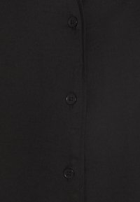 Camicia nera con bottoni, realizzata in un tessuto morbido, sei bottoni scuri sul davanti e una finitura pulita e sartoriale.