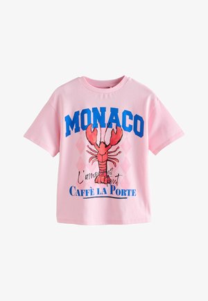 Roze T-shirt met korte mouwen, blauwe "MONACO" tekst, een rode kreeftafbeelding en Franse zinnen "L'amour est tout" en "Caffè La Porte" op de voorkant.