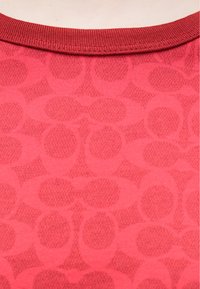 Czerwona tkanina o fakturze z wzorem przeplatających się kół. Prążkowany dekolt dodaje szczegółów gładkiej powierzchni.