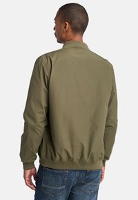 Giacca bomber verde oliva con zip frontale, polsini e orlo a coste. Texture morbida, design minimalista, con dettagli sulla parte posteriore.