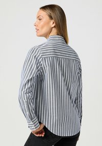 Randig skjorta i grått och vitt, med krage och långa ärmar, samt en rundad nederkant och lätt tygstruktur.