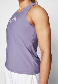 Lila ärmlös sporttopp med rund halsringning, tillverkad av mjukt tyg. Har en subtil logotyp fram och sydda sömmar.