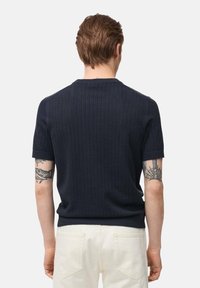 Marineblauwe geribbelde trui met korte mouwen en een ronde hals. Bevat een textuurstof. Gemaakt met lichte broek. Achteraanzicht.