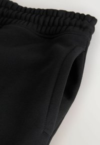 Schwarze Jogginghose mit einem elastischen Bund und seitlichen Taschen. Der Stoff ist glatt mit einem leichten Schimmer und zeigt ein figurbetontes Design.