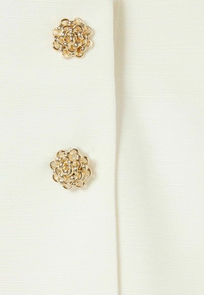 Tela blanca con dos adornos en forma de flor dorados y un detallado intrincado. Superficie texturizada con un sutil brillo.