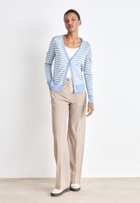Cardigan a righe blu e bianche con scollo a V, chiusura a bottoni e polsini a costine, abbinato a pantaloni beige chiaro a gamba larga e sneakers crema.
