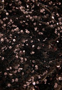 Tela marrón cubierta de lentejuelas circulares superpuestas, principalmente en tonos de oro rosa, con una superficie texturizada y hilos negros visibles.