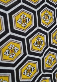 Patroonstof met hexagonale vormen in zwart, geel en wit. Bloemontwerp met oranje accenten op een gestructureerde achtergrond.