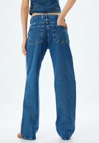 Vuoristavat siniset farkut, jotka on valmistettu denimestä, ja joissa on klassinen viiden taskun muotoilu sekä erottuva sivupaneelien yksityiskohtaisuus.