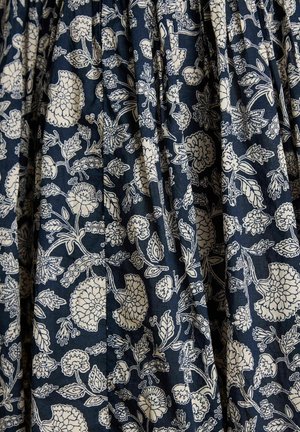 Material bleumarin cu un model floral alb, având diverse flori și frunze dispuse într-un design repetitiv cu pliu.