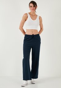 Marineblauwe wijde broek gemaakt van lichtgewicht stof met een elastische tailleband en een trekkoord. Gecombineerd met een getailleerde witte cropped tanktop.