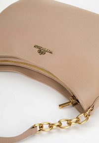 Borsa a mano in pelle beige con superficie texture, hardware dorato, cerniera prominente e dettaglio della tracolla a catena. Logo visibile sul fronte.