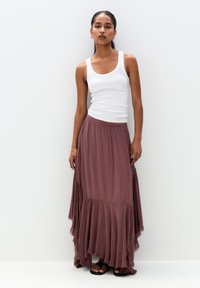 Long mauve skirt with ruffled hem, made of soft fabric. Paired with a fitted white tank top and worn with flat sandals.