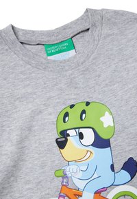 Šedé bavlněné tričko s kreslenou postavičkou v zelené helmě na oranžském kole. Na štítku je nápis "United Colors of Benetton".