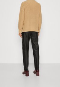 Suéter beige de punto acanalado con cuello alto y aberturas laterales, combinado con pantalones de cuero negros y zapatos burdeos de tacón grueso.