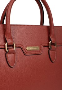 Sac à main en cuir marron texturé avec deux poignées supérieures, des accessoires en or et un détail en plaque. Il présente un design structuré et une forme allongée.