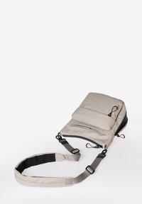 Beige gepolsterter Rucksack mit schwarzen Akzenten, verstellbaren Trägern und Reißverschlüssen. Verfügt über mehrere Fächer zur Aufbewahrung. Strukturierte Außenseite.