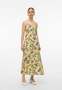 Robe maxi florale avec des bretelles spaghetti, en tissu jaune orné de motifs vibrants de fruits et de fleurs, un corsage ajusté et une jupe fluide.
