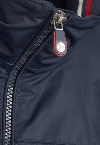 Granatowa kurtka zapinana na zamek błyskawiczny z metalowym uchwytem zamka w kolorze srebrnym oraz pomarańczowym akcentem, wykonana z fakturowanej tkaniny. Wnętrze zdobi wzór w paski.