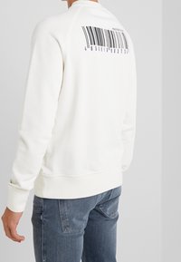 Sudadera blanca de algodón con cuello y puños de canalé. Presenta un gráfico de código de barras en negro y morado en la parte posterior.