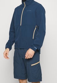 Marinblå lättviktsjacka med dragkedja fram och beige detaljer, matchad med koordinerande shorts med sidofickdragkedja.