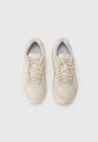 Beige sportovní boty vyrobené z prodyšné tkaniny a syntetických materiálů, s texturovanou podrážkou, šněrováním a reflexními prvky. Pohled z vrchu.