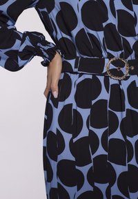 Niebieska sukienka w duże czarne kropki. Posiada bufiaste rękawy oraz pasek w talii z okrągłą metalową sprzączką. Teksturowany materiał.