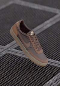 Brown and tan Nike low-top sneaker with laces, displayed above a metal grid surface.