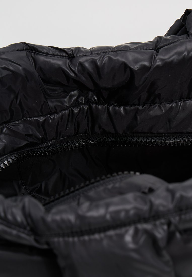 Schwarze Pufferbag-Innenausstattung mit einem reflektierenden Nylon-Textur, gerafftem Rand und einem Reißverschluss an der Oberseite für sichere Aufbewahrung.