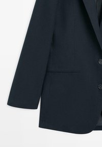 Donkerblauwe op maat gemaakte blazer met inkeping revers, twee knopen en een horizontale steekzak aan de rechterkant, zichtbaar tegen een witte achtergrond.