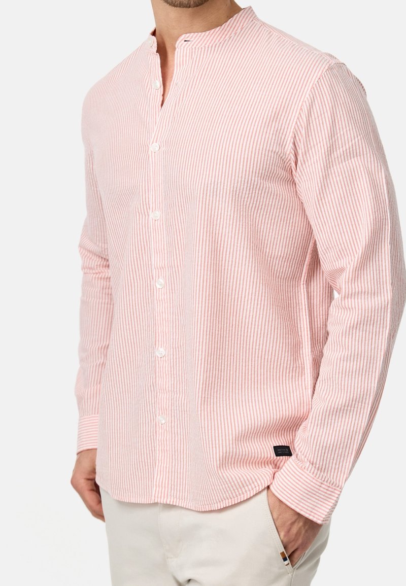 Camicia a maniche lunghe con colletto, di colore rosa chiaro con strisce verticali bianche, dotata di bottoni sul davanti e di una piccola etichetta sul lato inferiore.