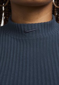 Jūrinės mėlynos juostelės megztinis su aukštu kaklu ir siuvinėtu juodu Nike logotipu ant apykaklės.Švelni tekstūra ir prigludusi išvaizda.